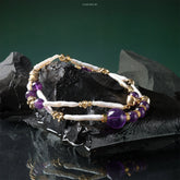 Amethyst Peaceful Muse Necklace with purple amethyst and white pearl beads on gold accents displayed on black stones.
